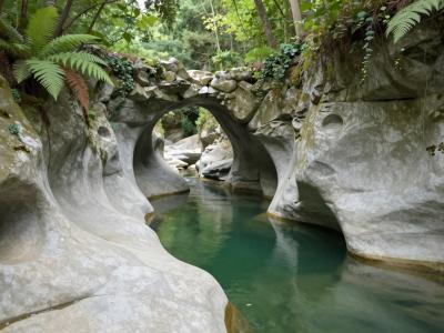 AI-generated illustration of Krčnik and Kotline, a natural water-polished stone arch over a creek with sculpted potholes and green pools in Goriška Brda