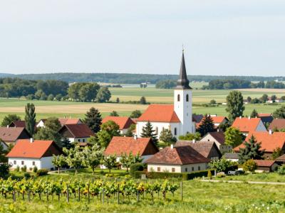 AI-generated illustration of Razkrižje, a small Pannonian village in Pomurje with its white church spire, red-roofed houses and vineyards above the Mura plain