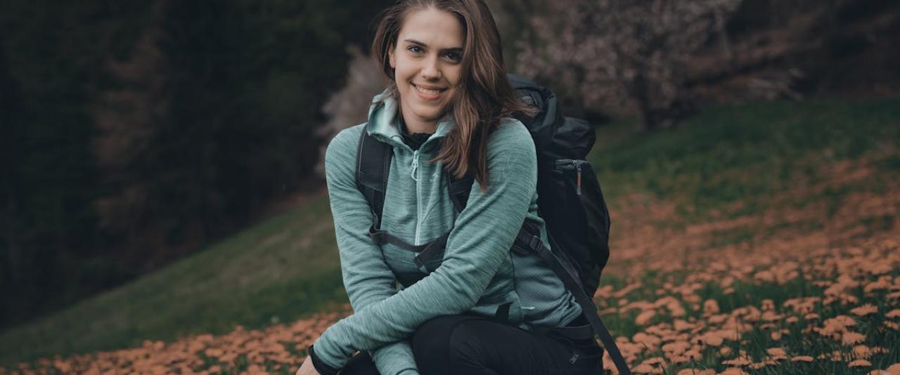 Teen girl with backpack enjoys scenic meadow in Slovenia, surrounded by blooming wildflowers.