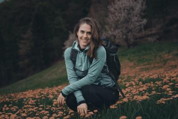 Teen girl with backpack enjoys scenic meadow in Slovenia, surrounded by blooming wildflowers.