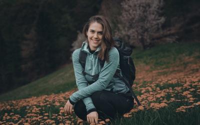 Teen girl with backpack enjoys scenic meadow in Slovenia, surrounded by blooming wildflowers.