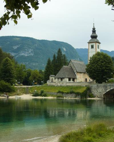 Free Beautiful view of a historic church and bridge in Bohinjska Bistrica, Slovenia, surrounded by nature. Stock Photo