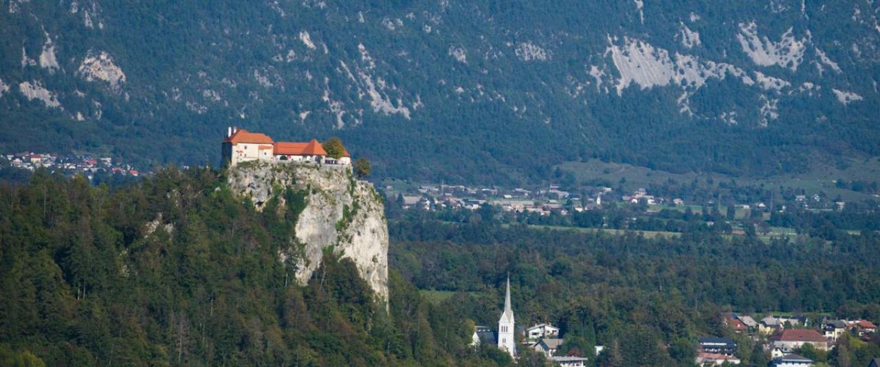 A stunning vertical shot of Bled Castle atop a cliff by Lake Bled with the Julian Alps in Slovenia.