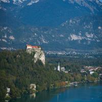A stunning vertical shot of Bled Castle atop a cliff by Lake Bled with the Julian Alps in Slovenia.
