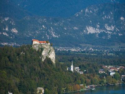A stunning vertical shot of Bled Castle atop a cliff by Lake Bled with the Julian Alps in Slovenia.