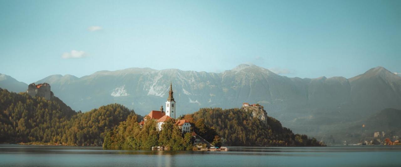Free Scenic view of Bled Island with a church in Lake Bled, surrounded by mountains, under a clear sky in Slovenia. Stock Photo
