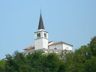 Gothic church tower rising above lush greenery under a clear blue sky in Kobarid, Slovenia.