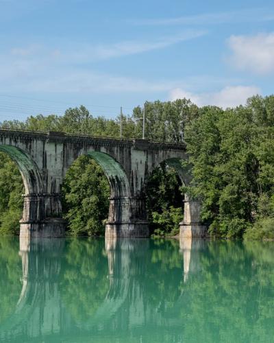 Beautiful arched railway bridge spanning across a serene river in Gorica, Radovljica, Slovenia, surrounded by lush greenery.