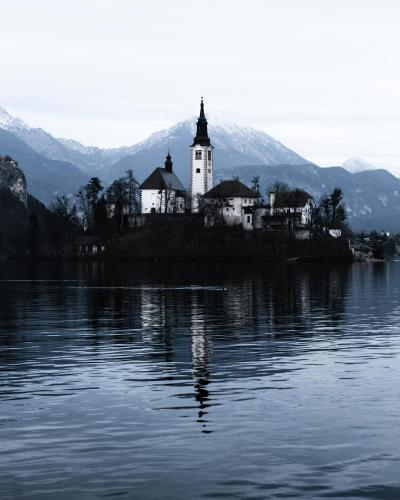 Free Enchanting winter view of Bled Island church reflecting in Lake Bled's tranquil waters. Stock Photo