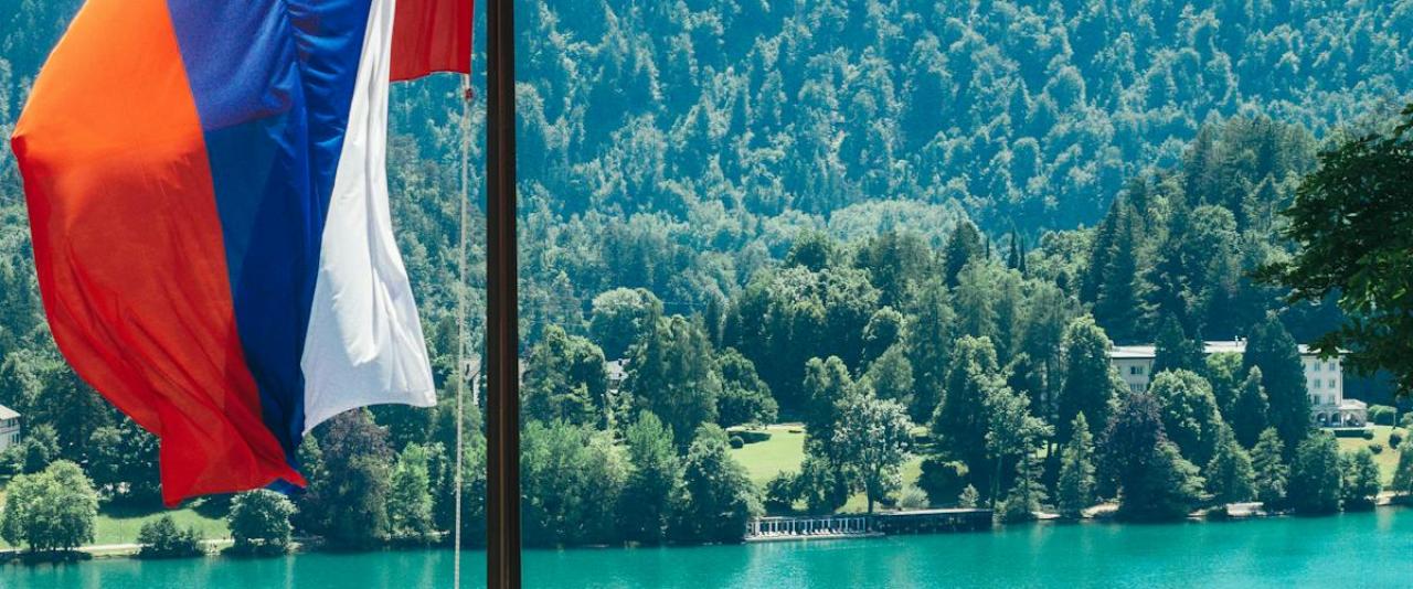 Serene Lake Bled view featuring Slovenian flag and lush mountains. Perfect for travel inspiration.