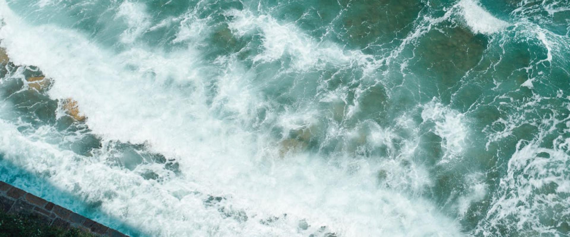 Beautiful aerial view of turquoise sea waves crashing on the rocky shore of Piran, Slovenia.