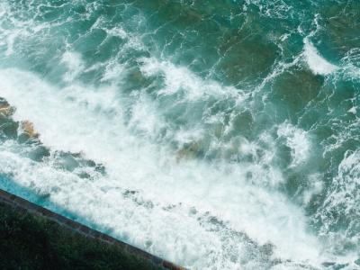 Beautiful aerial view of turquoise sea waves crashing on the rocky shore of Piran, Slovenia.