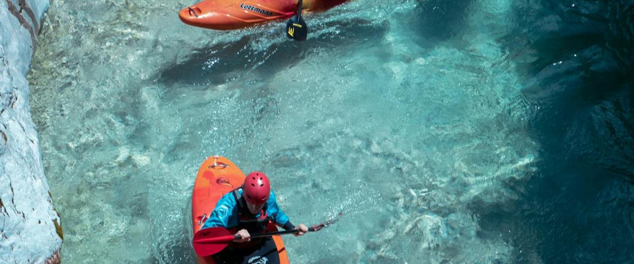 Free Three kayakers paddle through the stunning clear waters of the Soča River in Slovenia, showcasing adventure and nature. Stock Photo