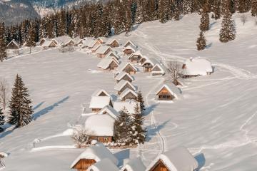 Charming wooden cabins blanketed in snow against a majestic mountain backdrop in Slovenia.
