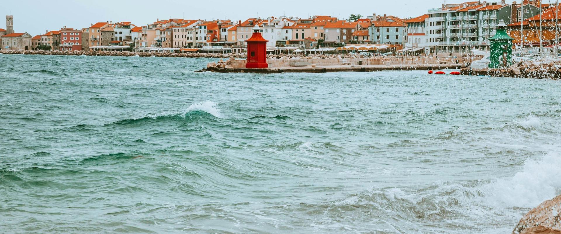 Picturesque coastal town of Piran, Slovenia, featuring vibrant houses and a red lighthouse by the Adriatic Sea.