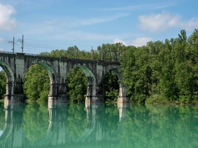 Beautiful arched railway bridge spanning across a serene river in Gorica, Radovljica, Slovenia, surrounded by lush greenery.