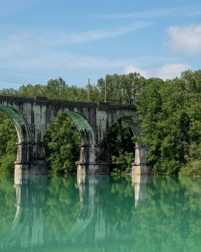 Beautiful arched railway bridge spanning across a serene river in Gorica, Radovljica, Slovenia, surrounded by lush greenery.