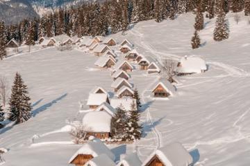 Free Charming wooden cabins blanketed in snow against a majestic mountain backdrop in Slovenia. Stock Photo