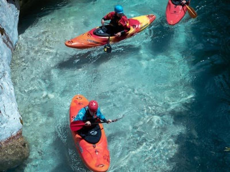 Free Three kayakers paddle through the stunning clear waters of the Soča River in Slovenia, showcasing adventure and nature. Stock Photo