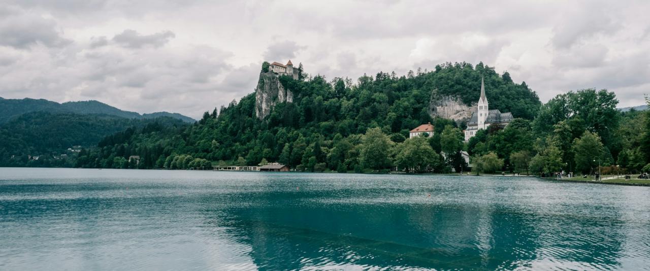 A wide shot of Lake Bled in Slovenia, featuring Bled Island with its Church of the Assumption and Bled Castle perched on a cliff in the background.