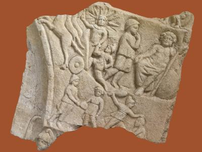 A photograph of a fragmented stone relief sculpture depicting mythological figures, including a sun god with radiating rays, a seated figure, and other human forms, set against a solid terracotta background.