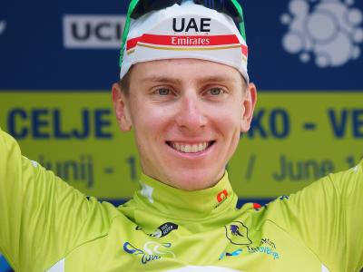 A close-up portrait of cyclist Tadej Pogačar in a yellow jersey and white UAE Team Emirates cap, with a blue and yellow backdrop displaying "UCI" and "CELJE" text.