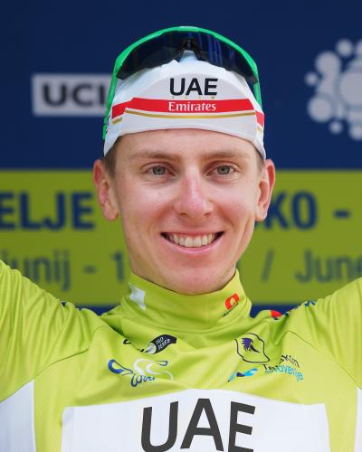 A close-up portrait of cyclist Tadej Pogačar in a yellow jersey and white UAE Team Emirates cap, with a blue and yellow backdrop displaying "UCI" and "CELJE" text.
