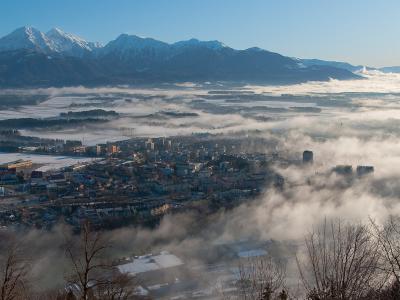 A panoramic view of Kranj, Slovenia, with the city nestled in a valley surrounded by snow-capped mountains and low-lying fog.