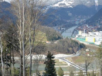 A high-angle landscape view showing a river valley with a bridge in the foreground, a town in the mid-ground, and a large industrial complex with a tall chimney on the right bank.