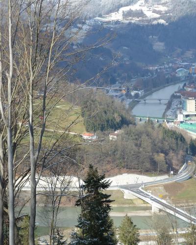 A high-angle landscape view showing a river valley with a bridge in the foreground, a town in the mid-ground, and a large industrial complex with a tall chimney on the right bank.