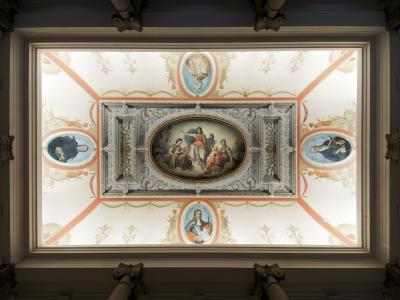 The image shows an ornate, painted ceiling with a central oval fresco depicting allegorical figures, surrounded by four oval portraits of historical men, framed by decorative stucco and painted garlands, viewed from below within a grand interior s
