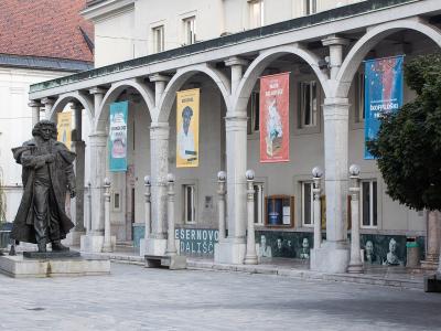 A stone arcade building with banners and a statue of a man in historical dress standing on a plinth in front.