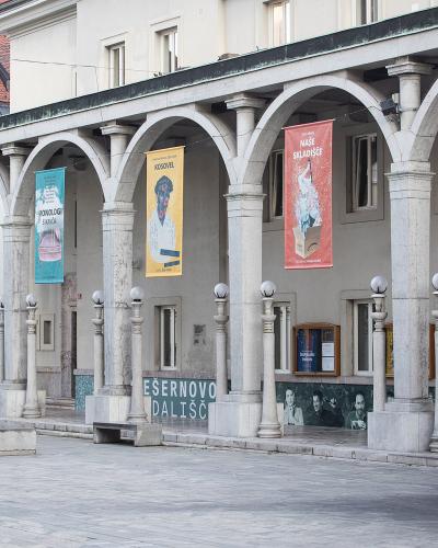 A stone arcade building with banners and a statue of a man in historical dress standing on a plinth in front.