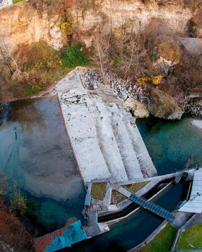An aerial fisheye view of a river gorge featuring a concrete weir or dam structure, a small building with a grey roof, and steep rocky cliffs with autumn foliage.