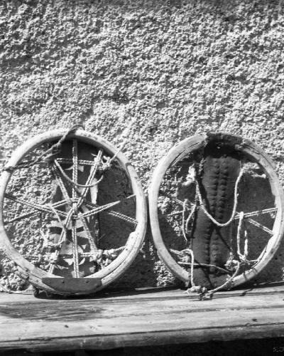 Two traditional wooden snowshoes (okrogla smuči) with rope bindings and a padded footrest, leaning against a rough stucco wall on a wooden ledge.