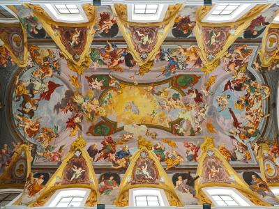 The image shows an ornate Baroque ceiling fresco with numerous figures, cherubs, and architectural illusions, featuring skylights and gilded stucco work.
