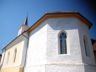 A low-angle shot of a white-washed church with a polygonal apse and a small spire against a blue sky.
