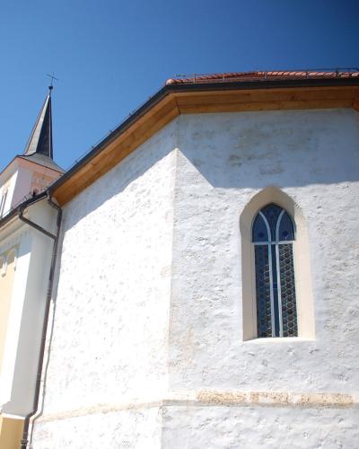 A low-angle shot of a white-washed church with a polygonal apse and a small spire against a blue sky.