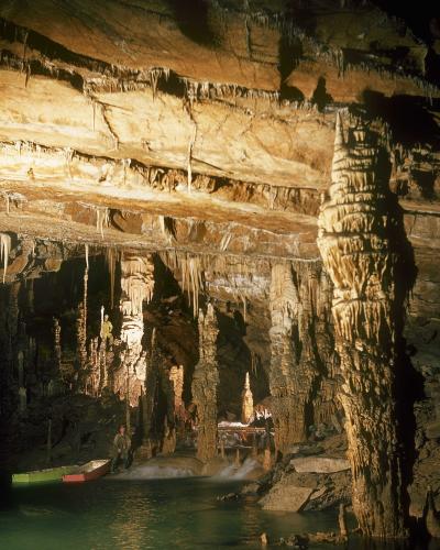 A caver wearing a red helmet and holding a camera is squeezing through a narrow, rocky cave passage.