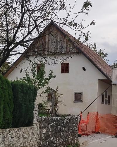 A white, two-story house with a steep gabled roof and wooden shutters, partially covered in scaffolding and protective sheeting for renovation, situated behind a stone wall and orange safety fencing.