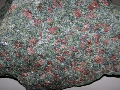 A close-up photograph of a rock specimen showing a greenish-grey matrix with distinct reddish-pink porphyroblasts, identified by the filename as kyanitic eclogite from the Pohorje Mountains.