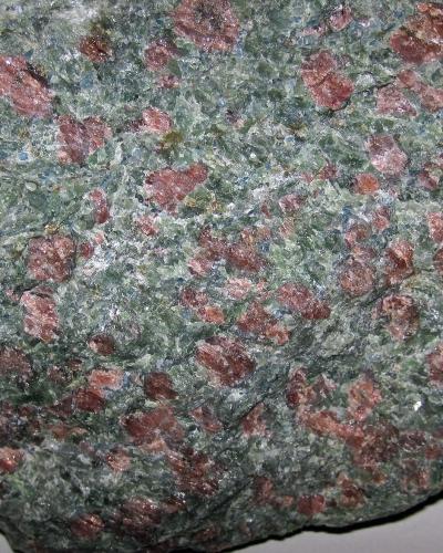 A close-up photograph of a rock specimen showing a greenish-grey matrix with distinct reddish-pink porphyroblasts, identified by the filename as kyanitic eclogite from the Pohorje Mountains.