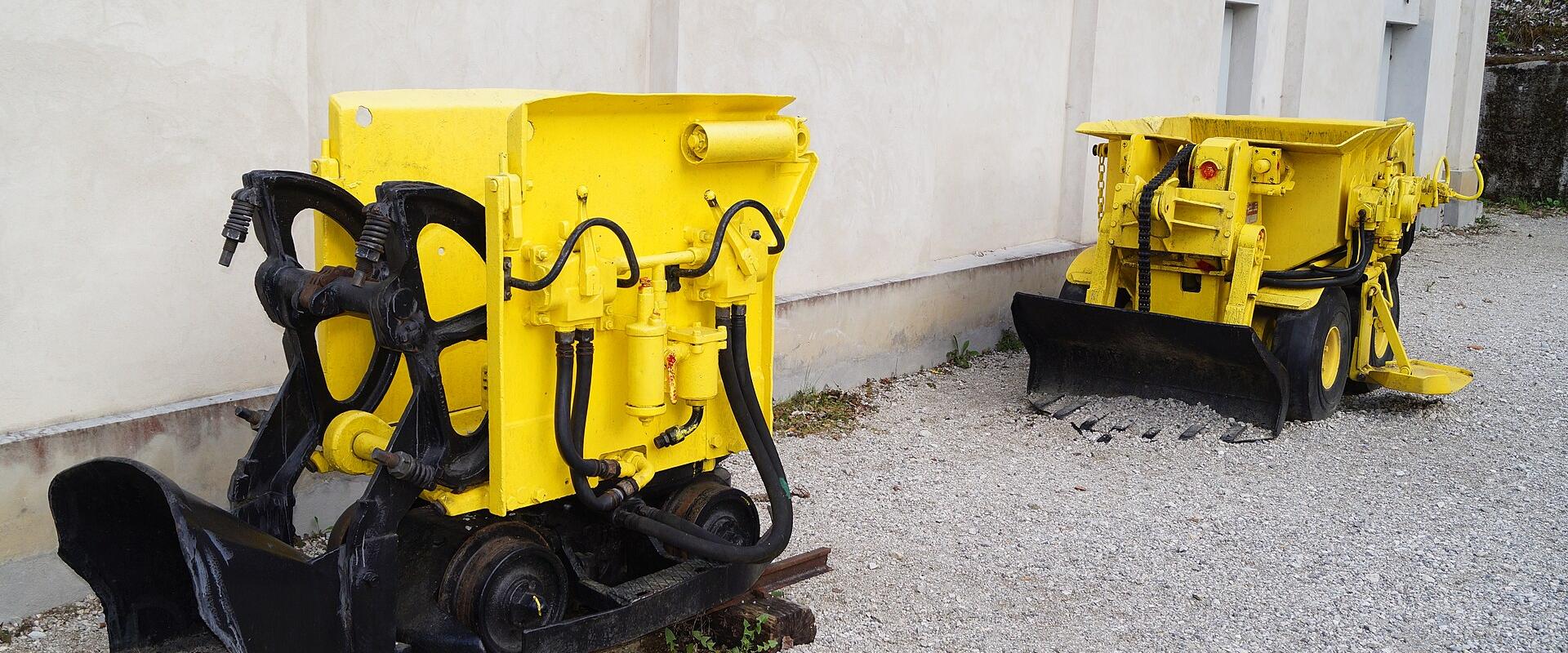 Two yellow industrial mining vehicles (track-mounted loaders) parked on a gravel surface next to a white building wall.