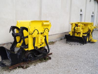 Two yellow industrial mining vehicles (track-mounted loaders) parked on a gravel surface next to a white building wall.