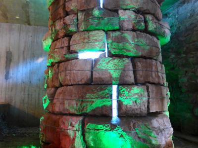 A cylindrical stone structure, likely a historic well or foundation pillar, illuminated with green and white lights inside a subterranean or basement-like space.