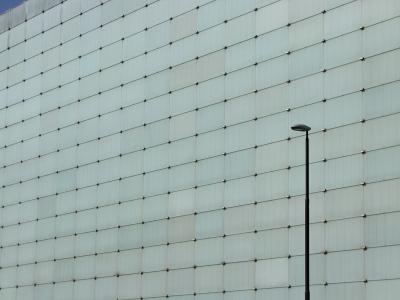 A close-up view of a modern building facade composed of a grid of light-colored rectangular panels with visible fasteners, and a single black street lamp post in the foreground.