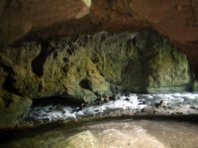 A view from inside a cave looking out towards a rushing underground river flowing through a rocky passage with moss-covered walls.