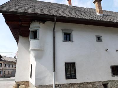 A white, two-story historic building with a slate roof, stone foundation, and a distinctive rounded corner turret, photographed from a street-level angle.