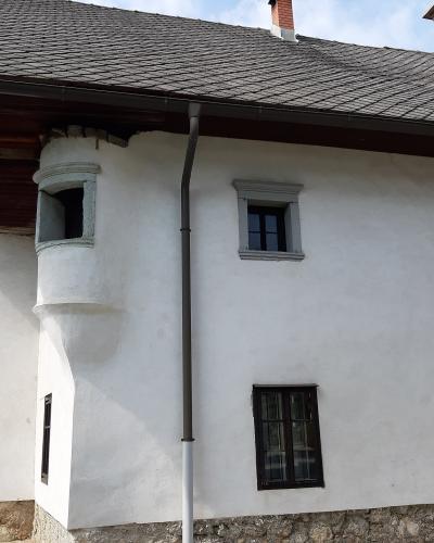 A white, two-story historic building with a slate roof, stone foundation, and a distinctive rounded corner turret, photographed from a street-level angle.
