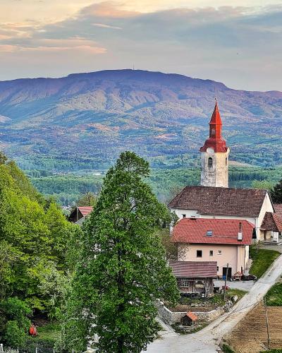 A white church with a red-tiled roof and steeple stands in a green, rural landscape with rolling hills and mountains in the background.
